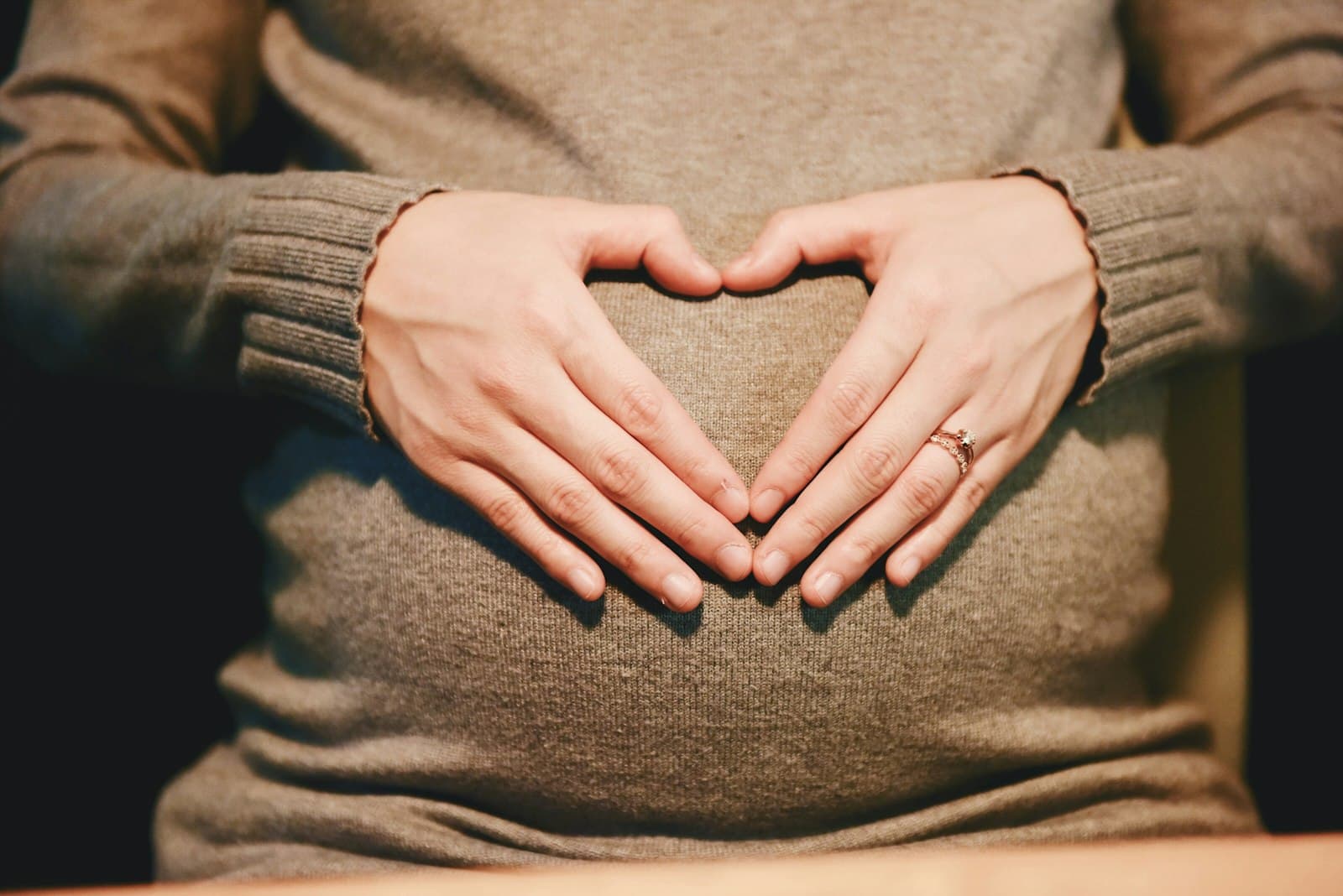 A pregnant woman resting both hands on her bump in a soft oatmeal knit