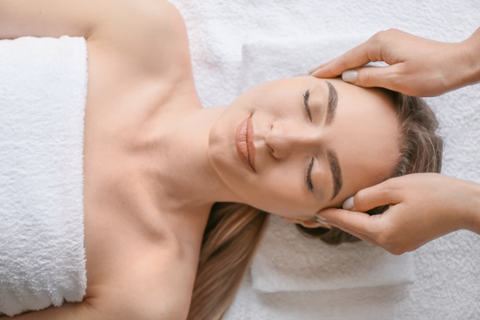A massage therapist's hands gently working at a relaxed client's head and temples